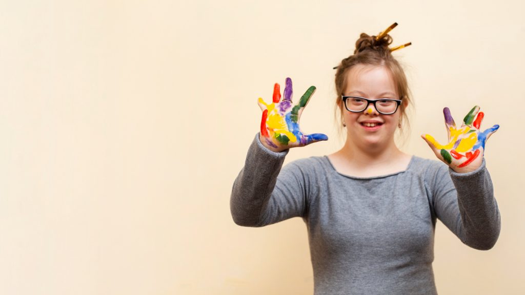 mulher com sindrome de down com as mãos pintadas de diversas cores